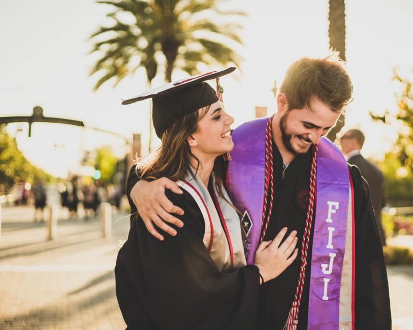 A graduate in cap and gown hugging a friend on graduation day