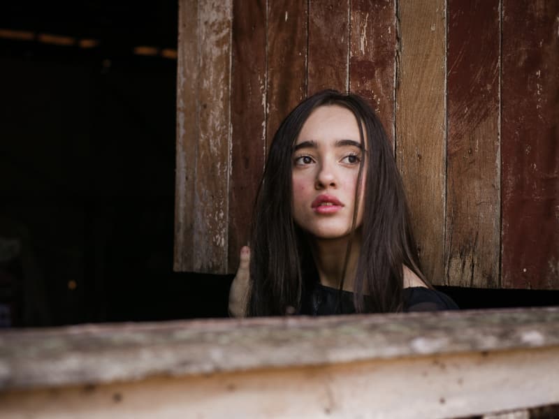 A young woman looking out thoughtfully from a wooden window