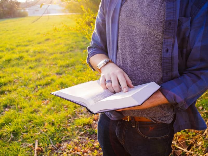 A student reading a book outdoors on a sunny lawn